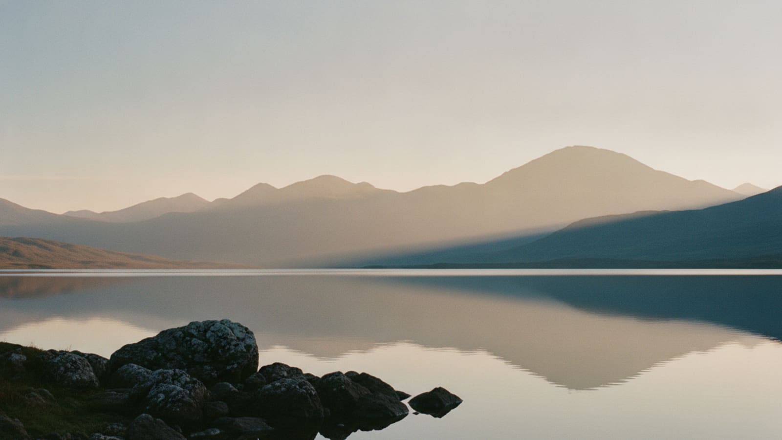 A still Highland loch at dusk, mountains reflected in the water